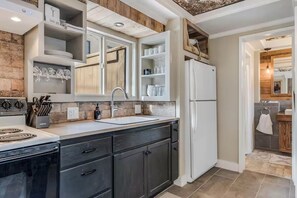 Eine Küche mit Einbauherd, Spüle und Kühlschrank. Es gibt Schränke und Regale mit Geschirr und Besteck.