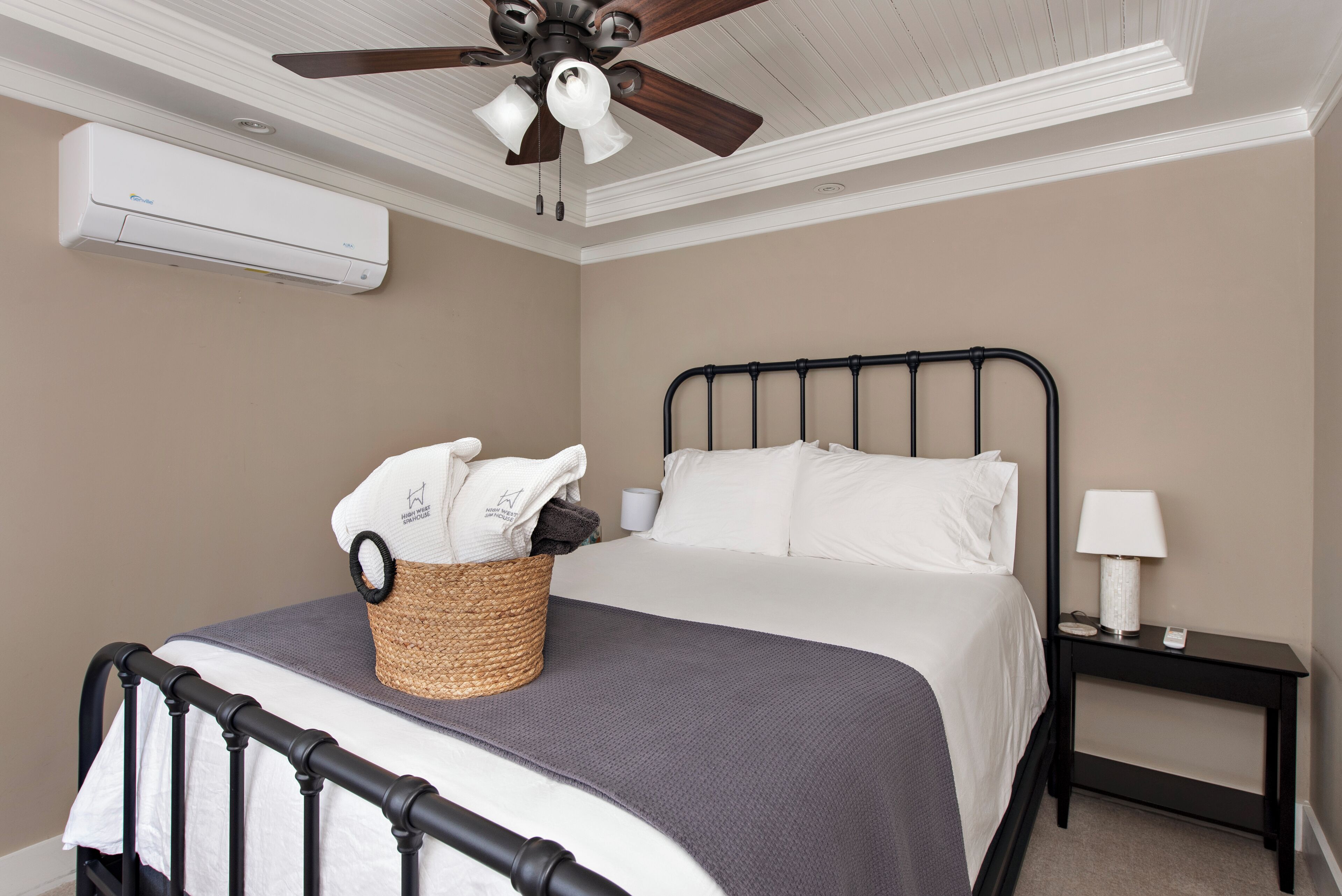 Een slaapkamer met een bed, nachtkastje, lamp, plafondventilator en airconditioning.