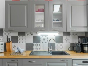 A kitchen with grey cabinets, a stainless steel sink, a coffee maker, and a Samsung oven. - Charming 2BR House Near Sea With Garden (Plouguerneau)