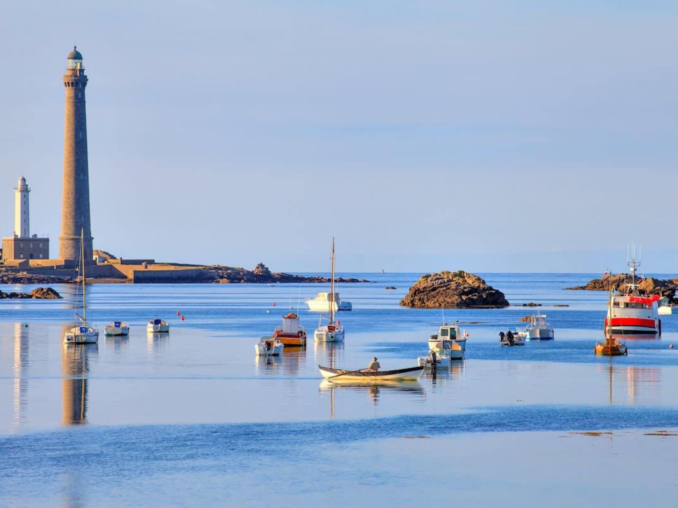 Un paysage côtier avec un phare, des bateaux et des affleurements rocheux.