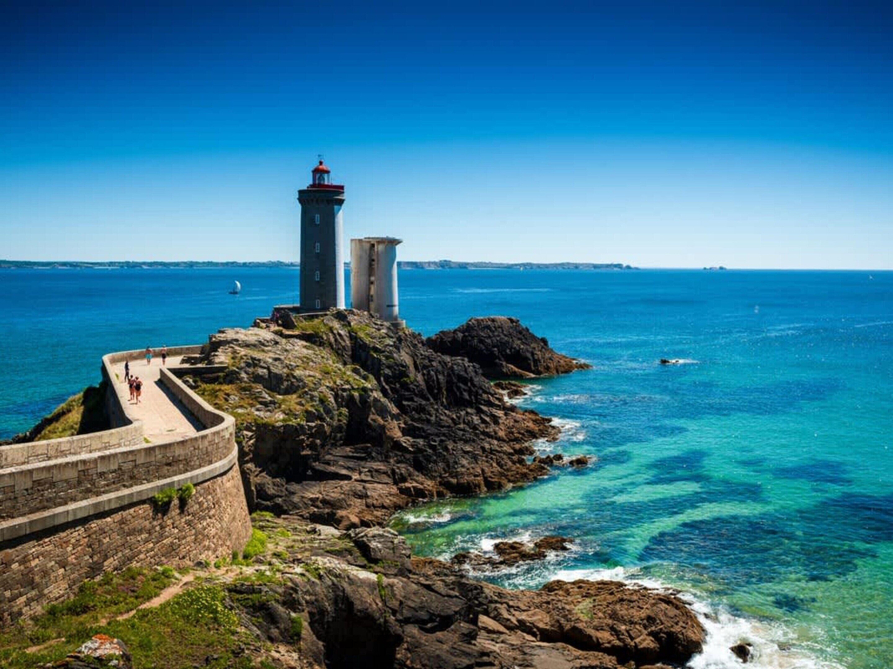 Ein Küstenleuchtturm mit einem steinernen Weg, der dorthin führt, mit Blick auf das Meer.