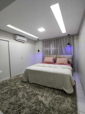 Un dormitorio con cama, ventilador de techo, aire acondicionado y ventana con cortinas.
