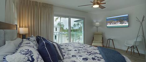 A bedroom with a bed, curtains, a ceiling fan, a window with a view, a chair, and a small table.