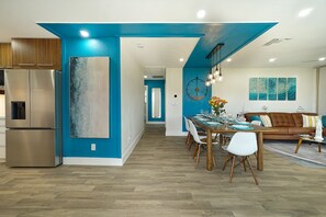 A modern kitchen with stainless steel appliances, a dining area with a wooden table and chairs, and a living room with a brown sofa and decorative wall art. - Renovated 4BD family beach retreat steps from the sandy beach of Bonita Springs (Bonita Springs)