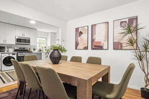 A modern kitchen with a dining area, including a wooden table and chairs, a microwave, oven, and a washing machine. - What A View! Relax in style. Private balcony enjoying NYC skyline views. (Jersey City)