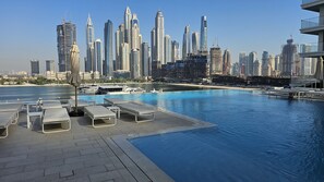 A poolside area with lounge chairs and a view of a city skyline with modern skyscrapers. - Modern Beachfront 3BR Apt | Near Marina & JBR (Dubai)