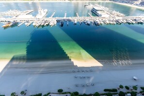 An aerial view of a marina with boats docked, a sandy beach, and a clear sky. - Modern Beachfront 3BR Apt | Near Marina & JBR (Dubai)