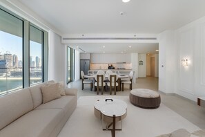 A modern living room with a sofa, ottoman, and round coffee table. A dining area with chairs and a table is visible in the background. - Modern Beachfront 3BR Apt | Near Marina & JBR (Dubai)