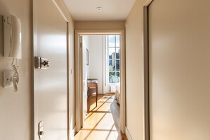 Ein Flur mit einer Tür zu einem Zimmer, das ein Bett und ein Fenster beinhaltet.