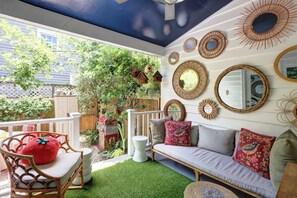 Eine gemütliche Terrasse mit einer weißen Couch, roten und grauen Kissen und einem Korbstuhl.