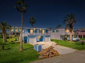 Un barrio residencial con una casa de dos plantas que tiene un balcón, un garaje y un césped cuidado con palmeras.