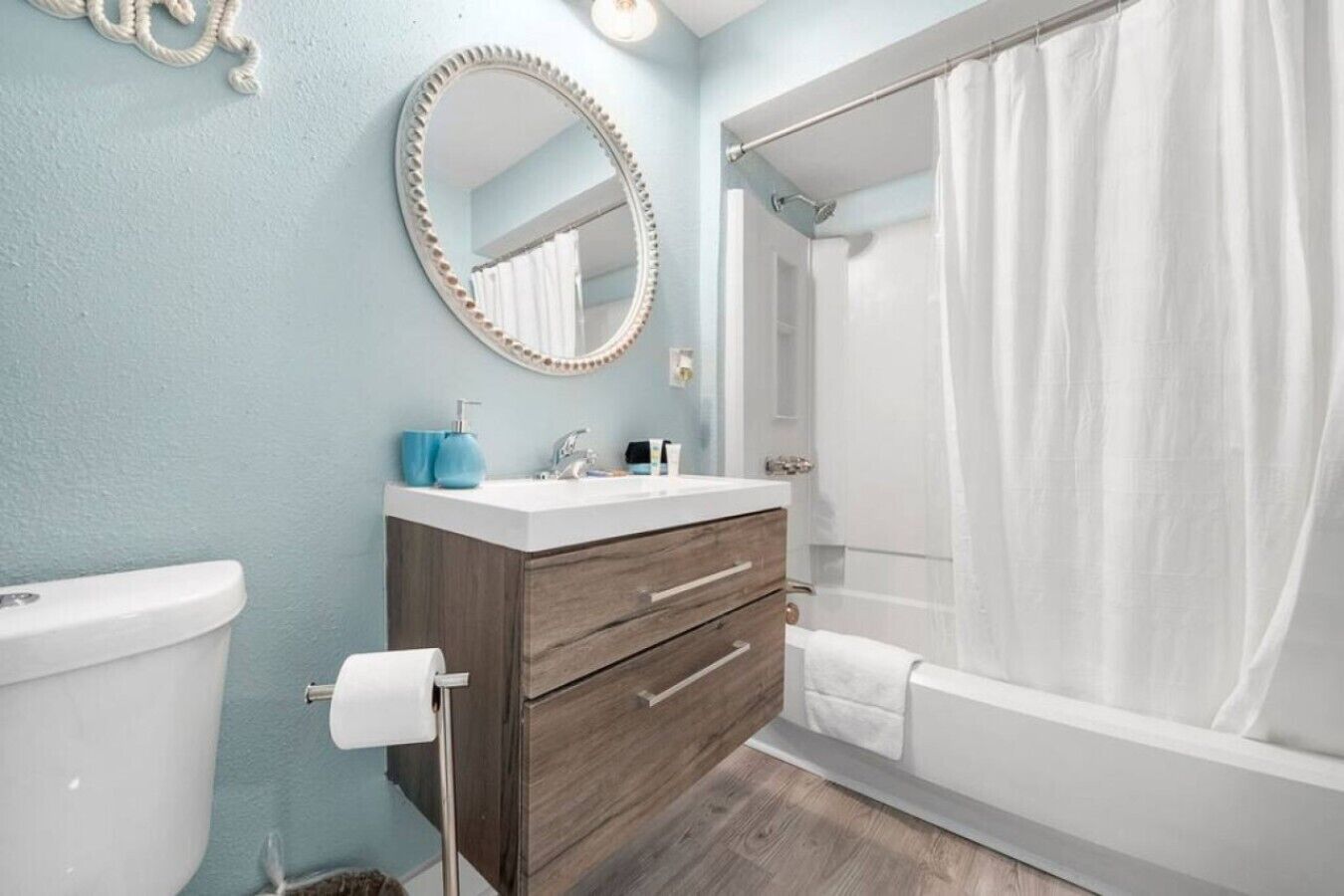 A bathroom with a toilet, sink, vanity, mirror, shower curtain, and a towel rack.