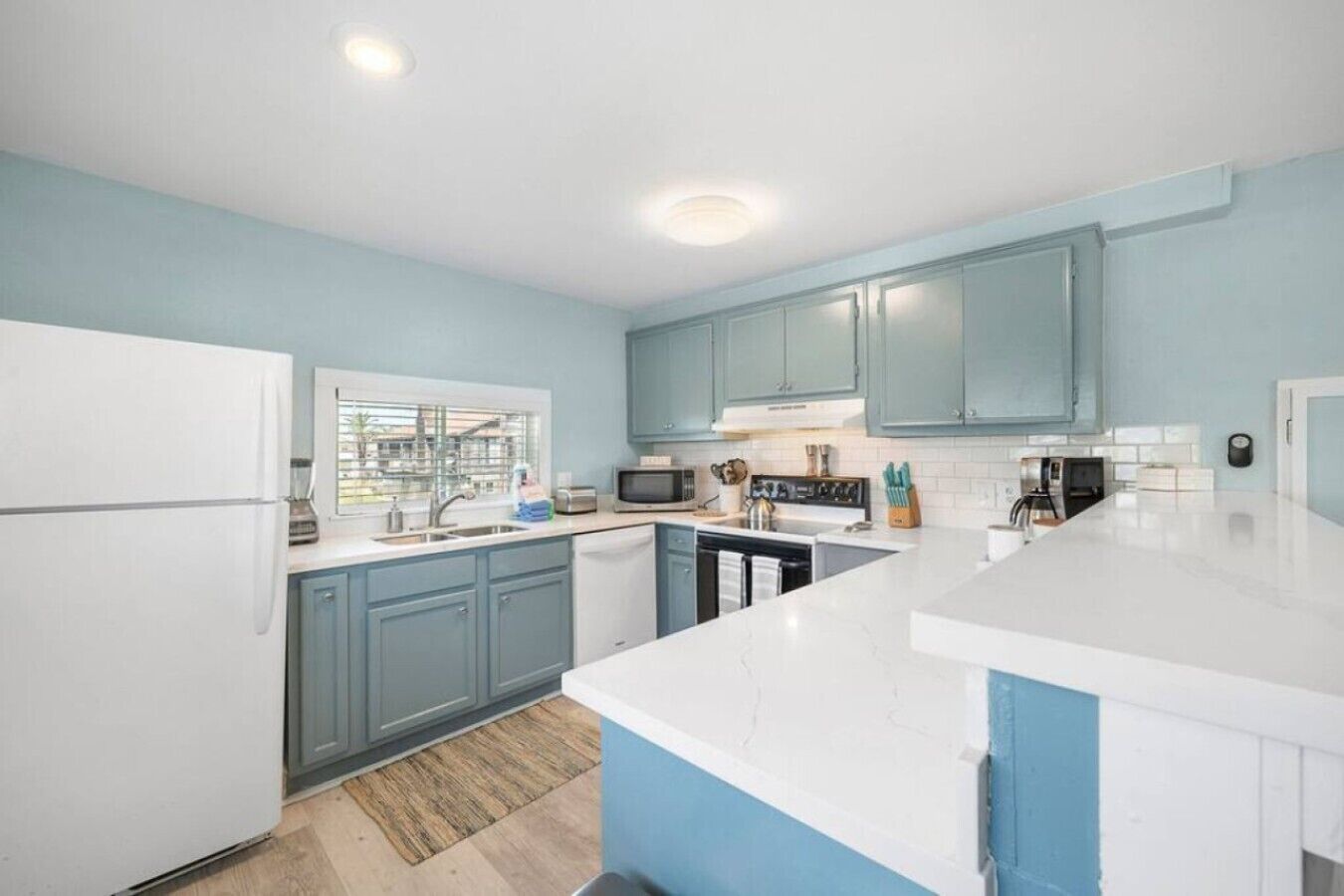 Une cuisine moderne avec des meubles bleu clair, des plans de travail blancs et un îlot central.