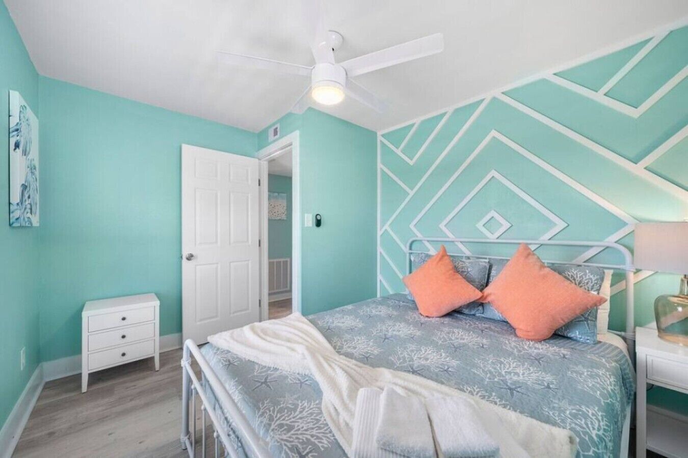 Ein Schlafzimmer mit einem Bett, einem Nachttisch, einer weißen Kommode, einem Deckenventilator und einer Tür zu einem anderen Raum.