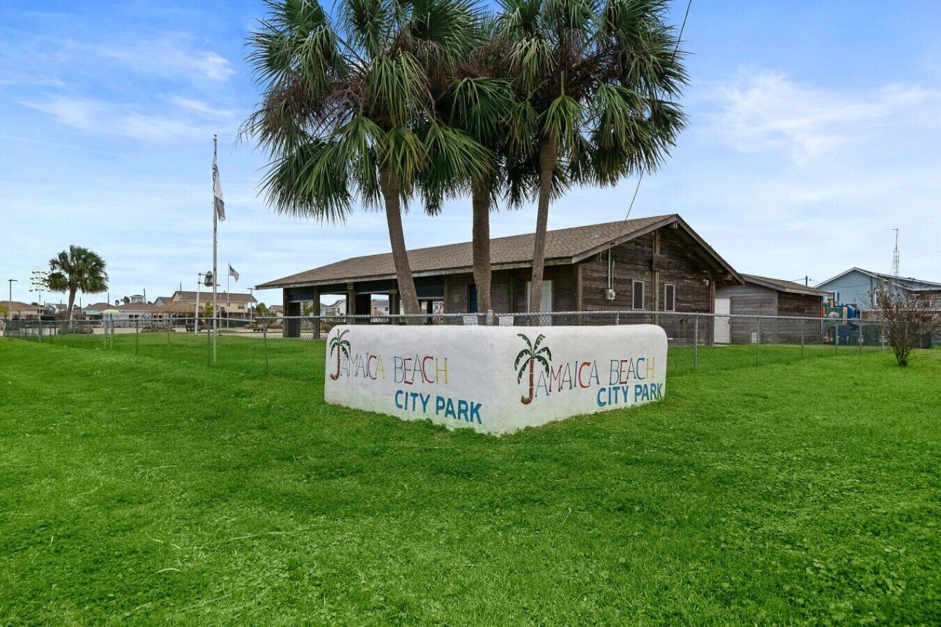 A sign for Jamaica Beach City Park with a building in the background.