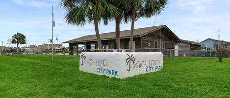 A sign for Jamaica Beach City Park with a building in the background.
