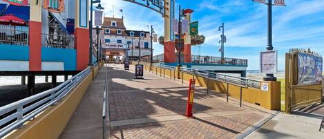 Un muelle de madera con la entrada a un muelle de diversiones, un cartel anunciando atracciones y un evento de Halloween.