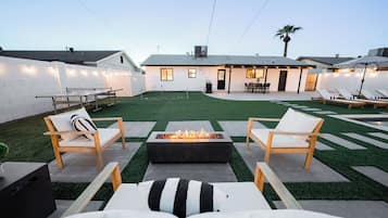 A backyard with a fire pit, lounge chairs, and a patio area.
