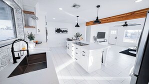 Une cuisine moderne avec des meubles blancs, un îlot central, des luminaires suspendus et une poutre en bois au plafond.