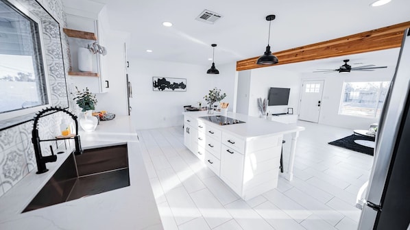 A modern kitchen with white cabinetry, a central island, pendant lighting, and a wooden ceiling beam.
