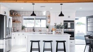 Une cuisine moderne avec des meubles blancs, des appareils en acier inoxydable, une grande fenêtre et un coin bar avec des tabourets.