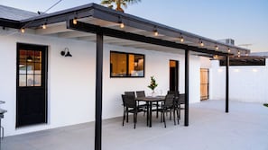 A covered patio with a table and chairs, a potted plant, and a window with a view.