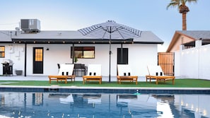 A modern house with a pool, outdoor seating, and a large umbrella.