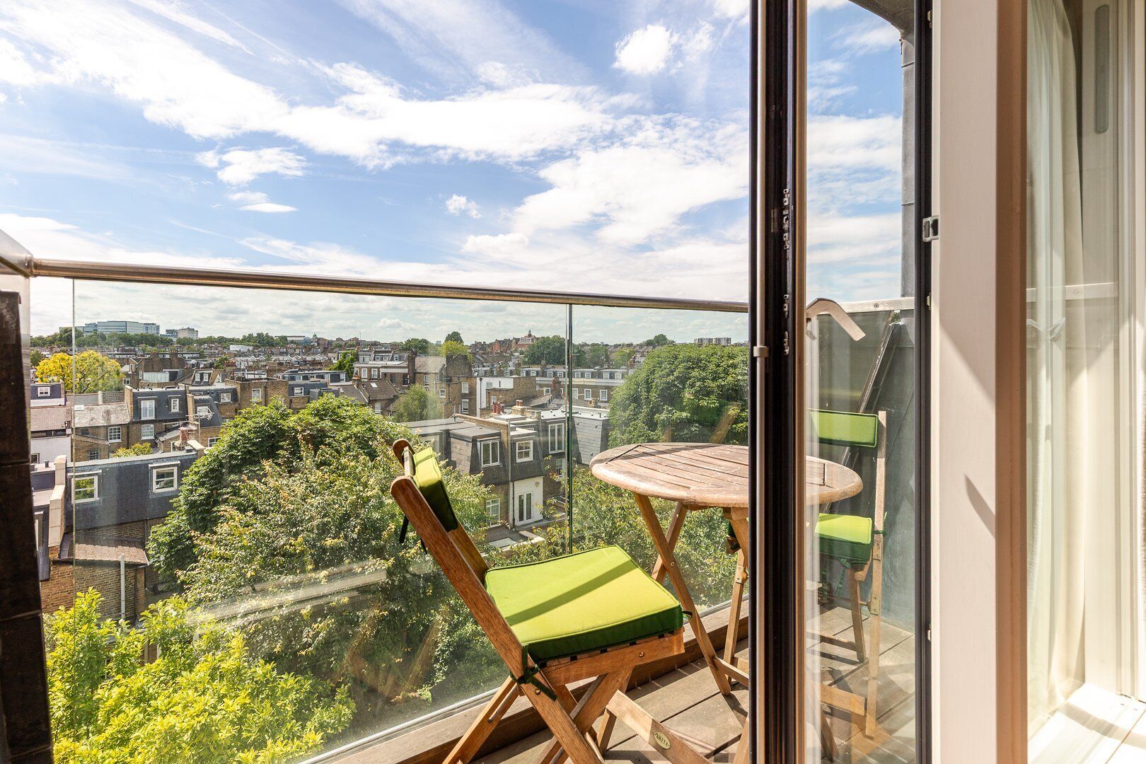 Ein Balkon mit Blick auf eine Stadtansicht, einem Holztisch und einem Sessel mit Kissen.