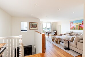 A modern living room with a sofa, a dining table, and a staircase leading to an upper floor. - Brook Green Flat by Kensington Olympia (London)