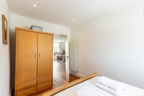 Ein Schlafzimmer mit einem Holzschrank, einem Bett mit weißer Bettwäsche und Blick in einen Essbereich.