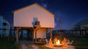 A covered outdoor area with a fire pit, seating, and a building in the background.