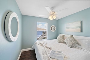 Un dormitorio con cama, ventilador de techo, reloj, ventana con vistas y un cuadro en la pared.