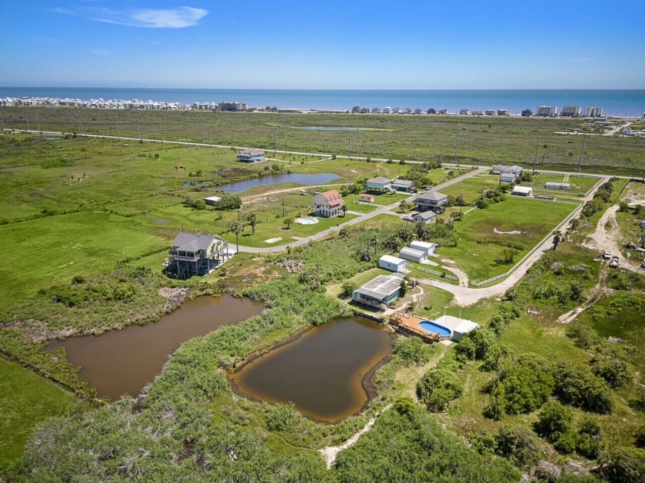 Oversigtsbillede af et boligområde med flere huse, en lille sø og frit udsyn til havet.
