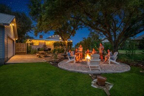 A backyard with a fire pit, outdoor seating, and a house in the background.