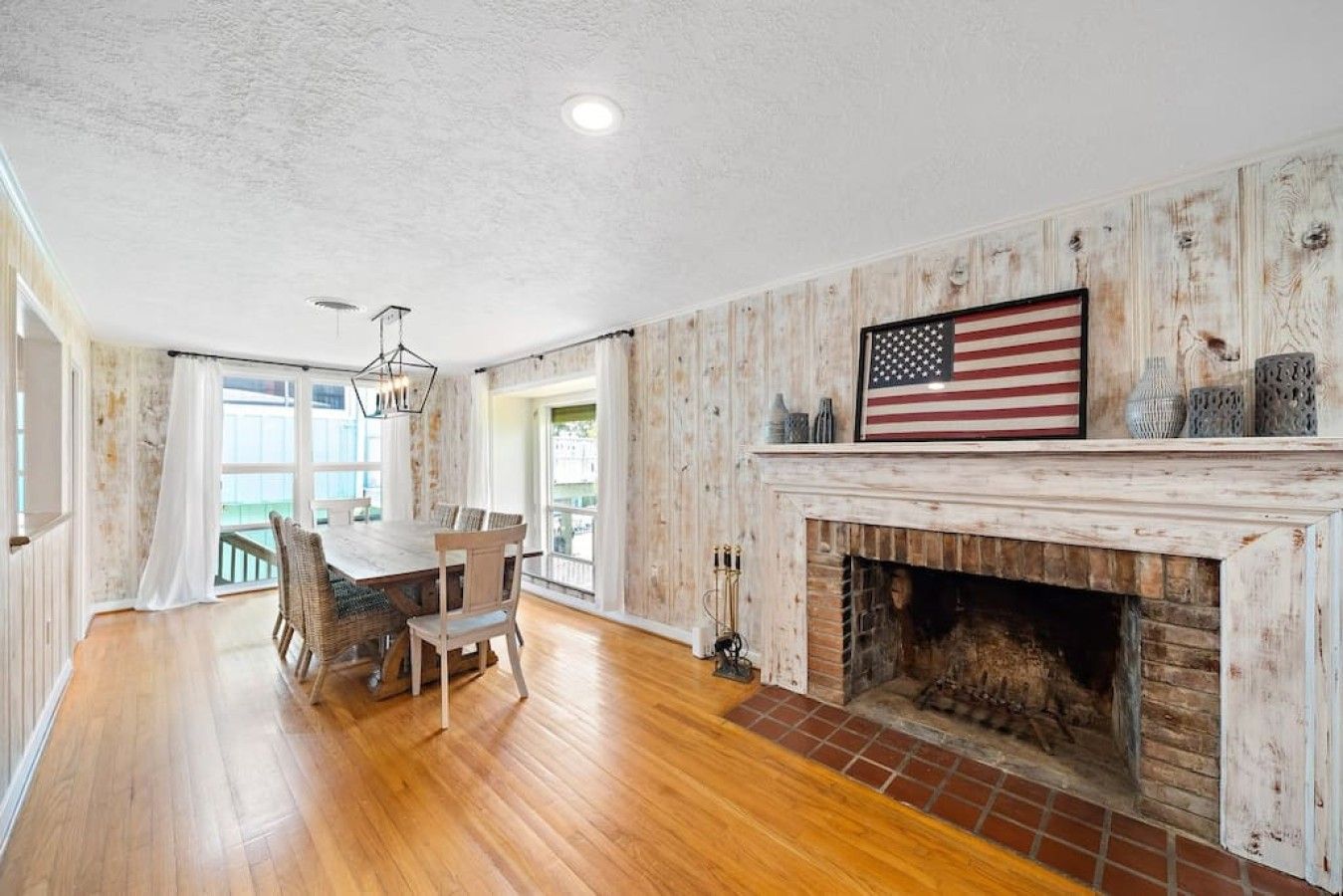 A spacious room with a wooden floor, a dining table with chairs, a fireplace, and an American flag decoration.