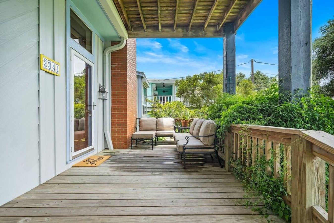 A wooden deck with outdoor seating, a brick wall, and a clear sky.