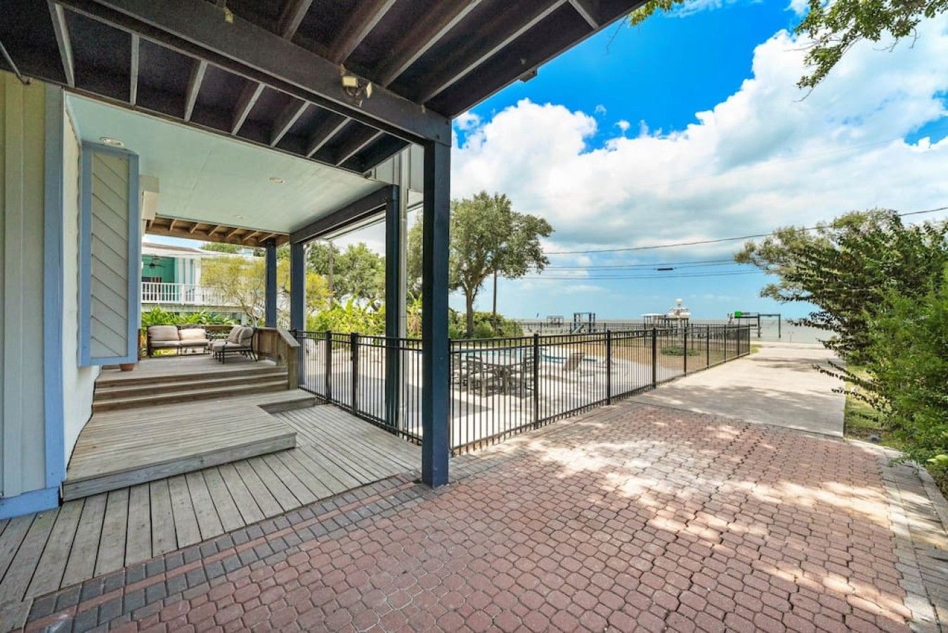 A covered outdoor area with a wooden deck, a brick pathway, and a metal fence.