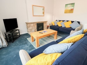 A living room with a TV, sofa, coffee table, fireplace, and a painting on the wall. - Sundale (Strathaven)