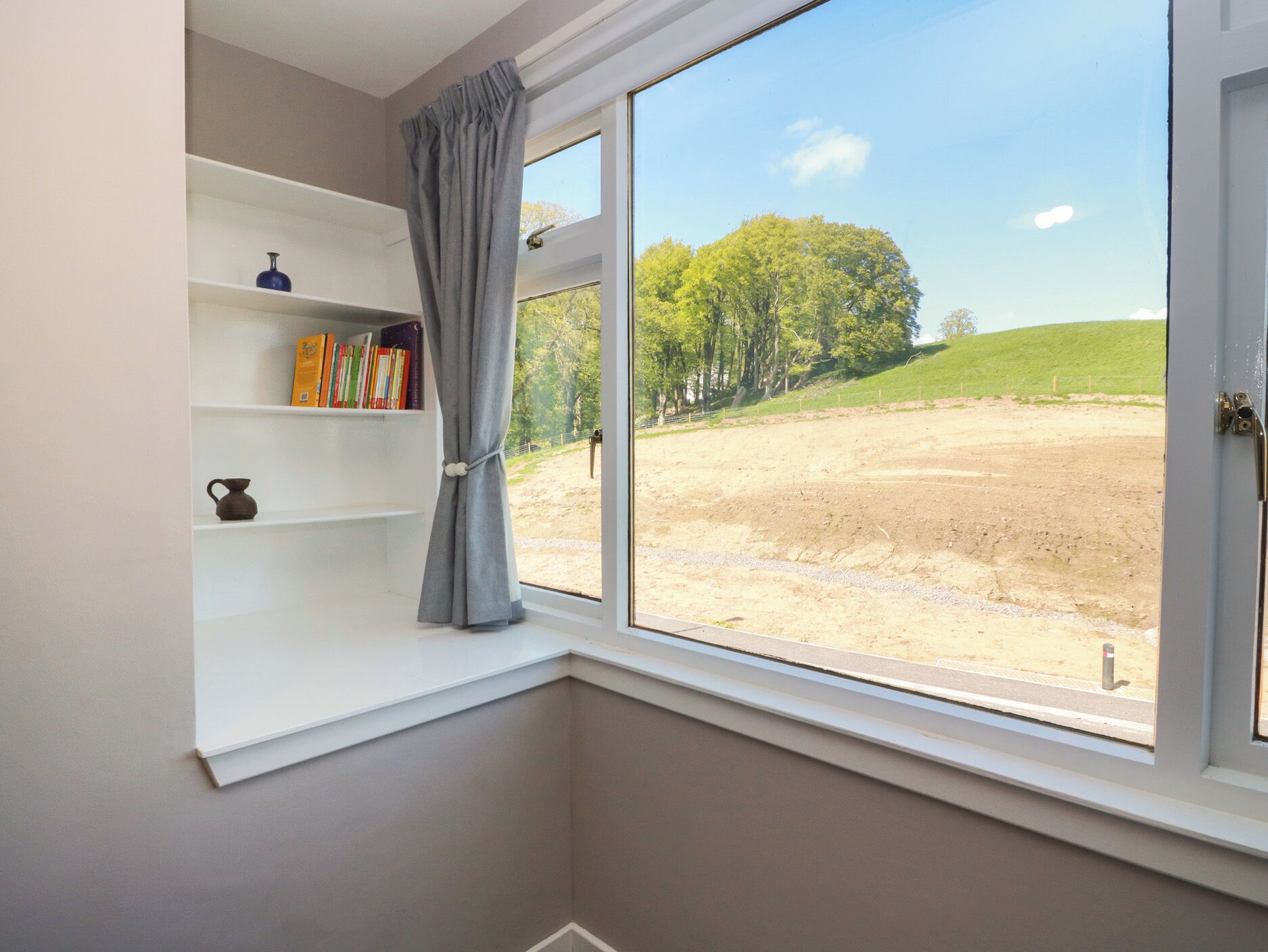 A room with a large window, a bookshelf, and a view of a grassy field.