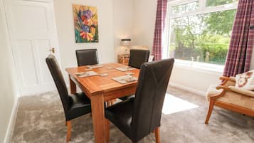 A dining area with a wooden table, black chairs, a painting on the wall, and a window with curtains.