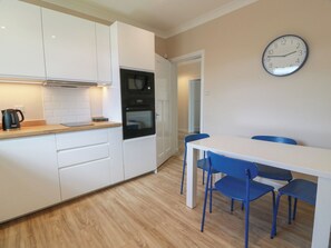 A modern kitchen with white cabinets, a black oven, a kettle, and a clock on the wall.