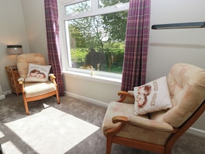 A room with two wooden armchairs, a small table, a window with curtains, and a lamp. - Sundale (Strathaven)