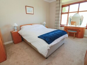 A neatly arranged bedroom with a bed, bedside tables, a dresser, a mirror, and a framed picture on the wall. - Sundale (Strathaven)