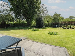 A grassy backyard with a patio table, a large tree, and a garden area. - Sundale (Strathaven)