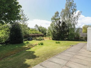 A well-maintained garden with a paved patio area, surrounded by mature trees and a variety of shrubs.