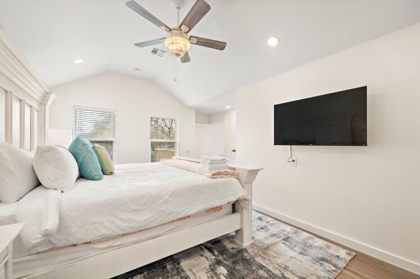 A bedroom with a bed, pillows, a ceiling fan, a TV, and a window with blinds.