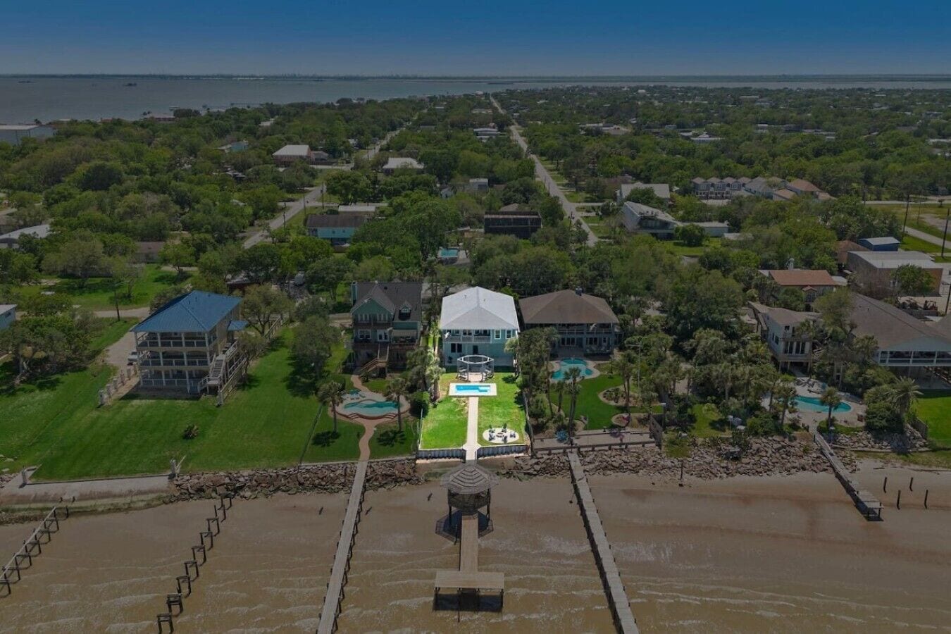 An aerial view of a residential area with houses, a large central building with a swimming pool, and a dock extending into a body of water.