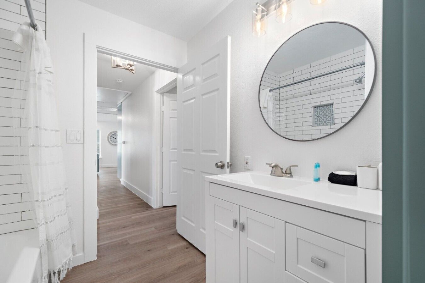 Un bagno moderno con un mobile lavabo bianco, uno specchio rotondo e una zona doccia.