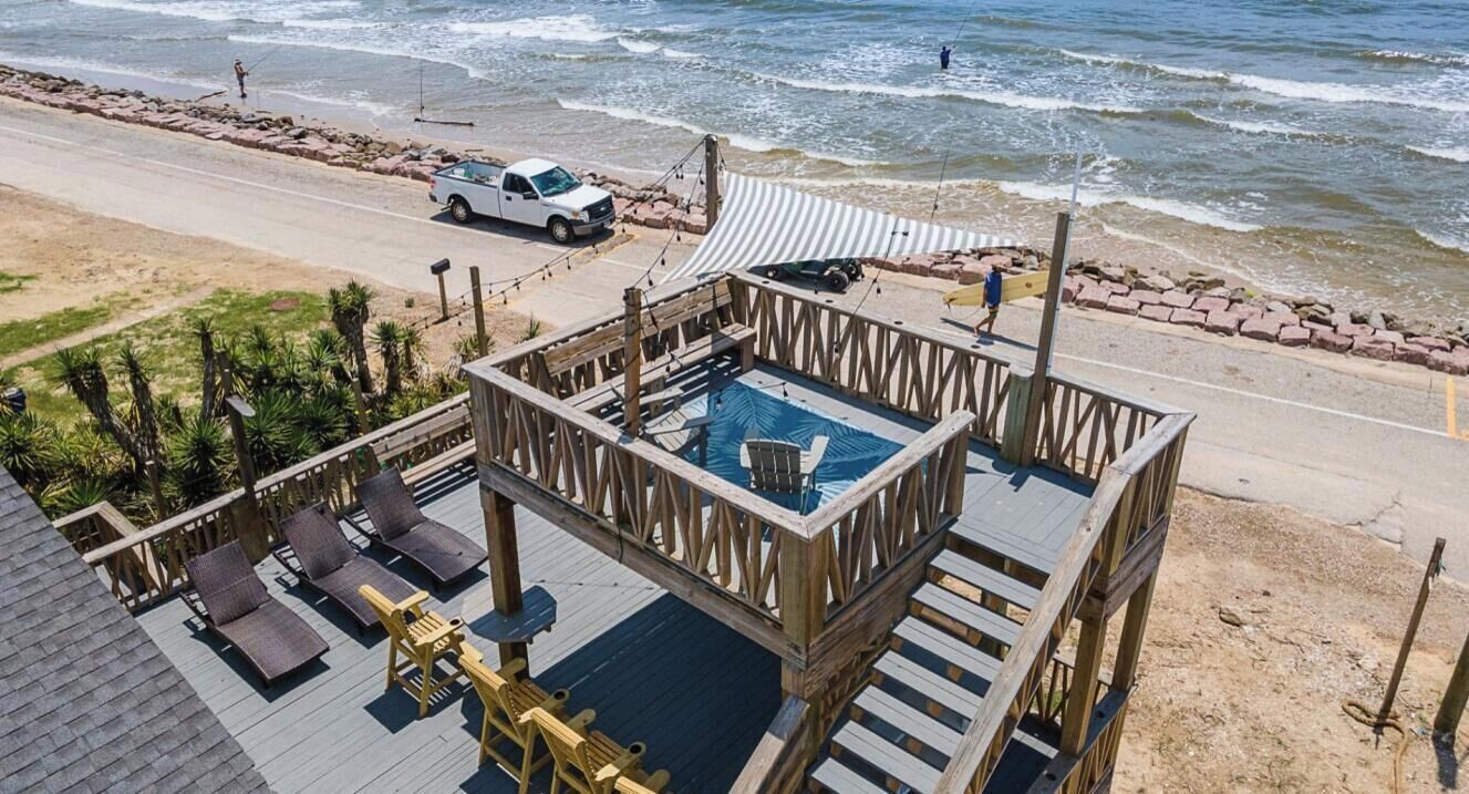 A wooden deck with a pool, lounge chairs, and a beach view.