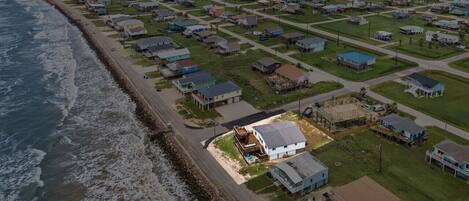 An aerial view of a coastal residential area with houses, a beach, and a road parallel to the shore.